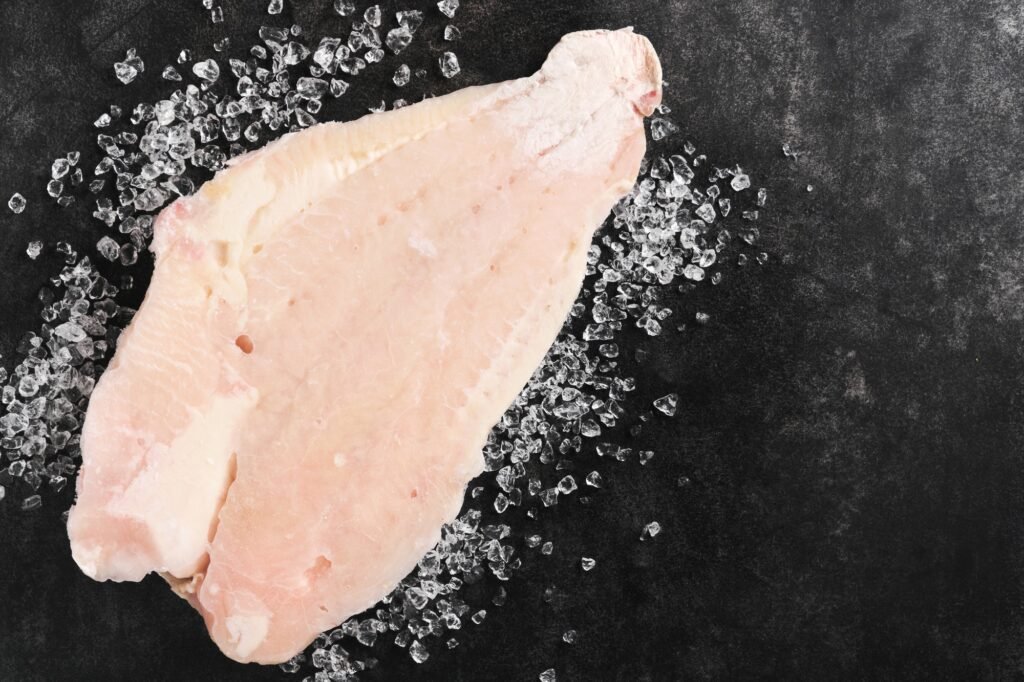 Pangasius frozen fillet. Raw fillet of white fish catfish. Pangasius with spices. Black background.